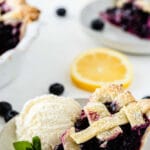 slice of blueberry pie on a white plate with a scoop of vanilla ice cream