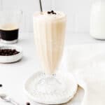 coffee milkshake in tall glass with a straw with a cup of coffee and milk in the background
