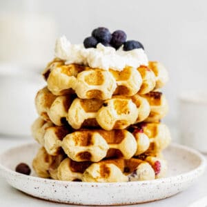 closeup of a stack of four waffles topped with whipped cream and fresh blueberries