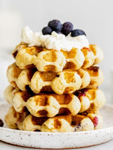 closeup of a stack of four waffles topped with whipped cream and fresh blueberries