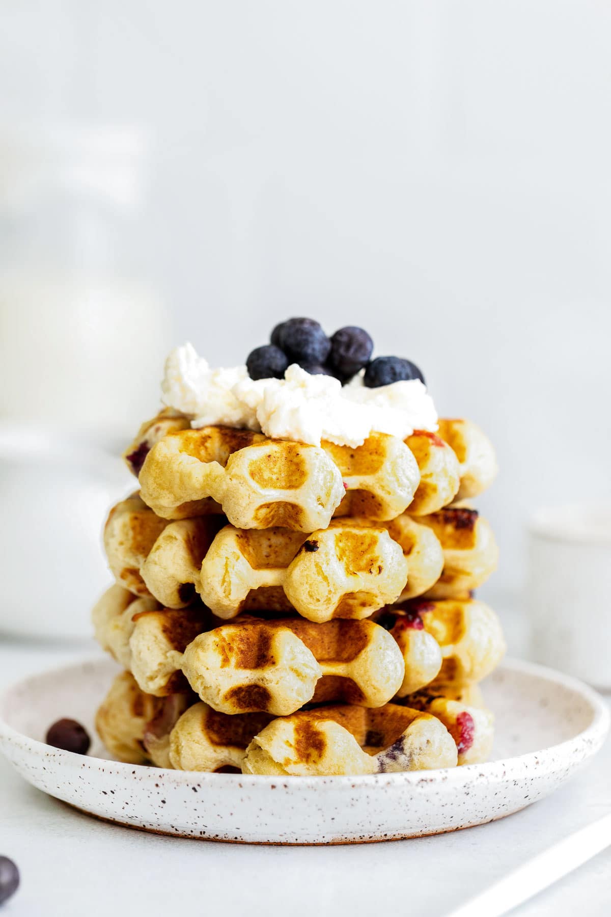 stack of four ricotta waffles topped with whipped cream and fresh blueberries
