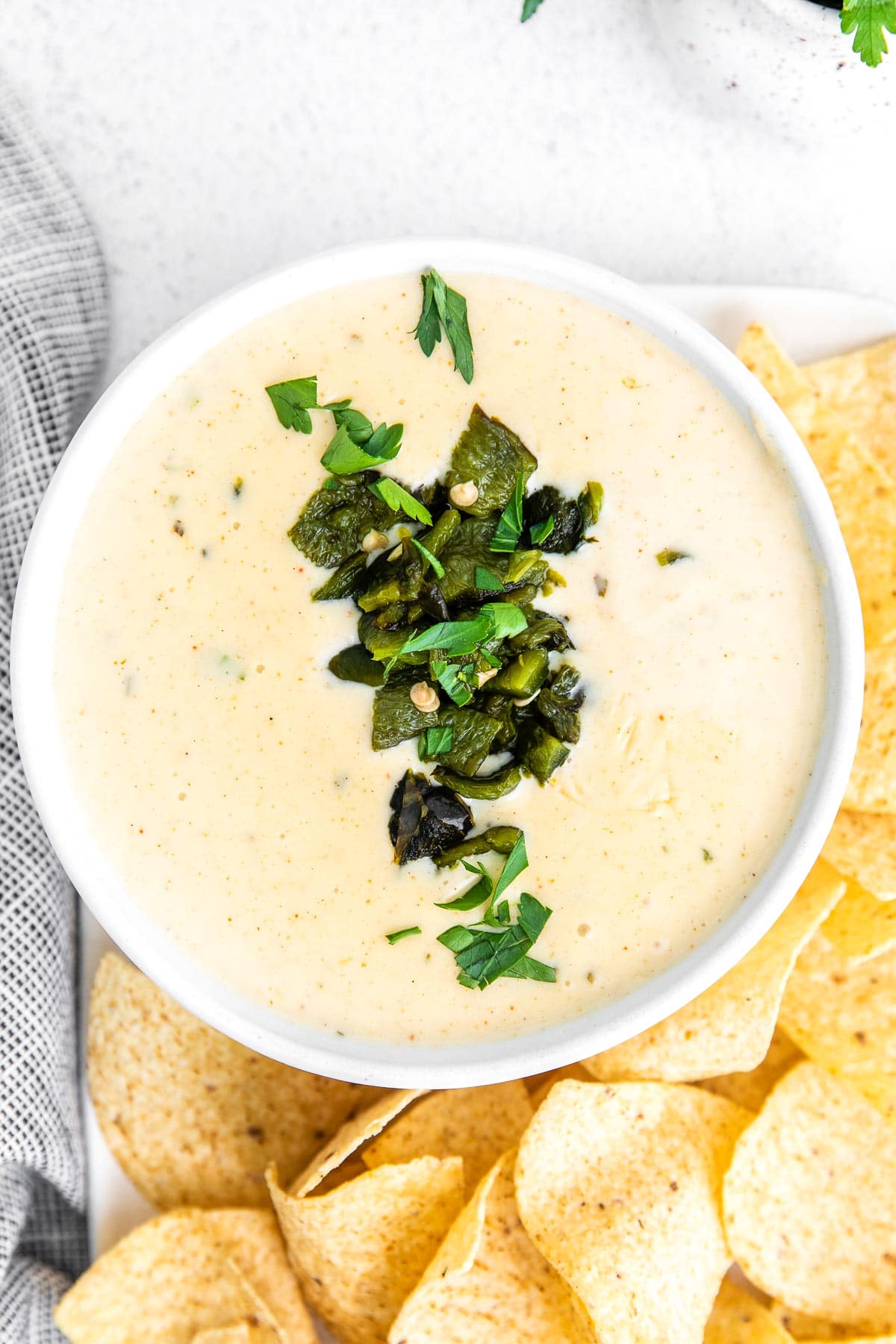 white queso dip in a white bowl topped with chopped poblano peppers