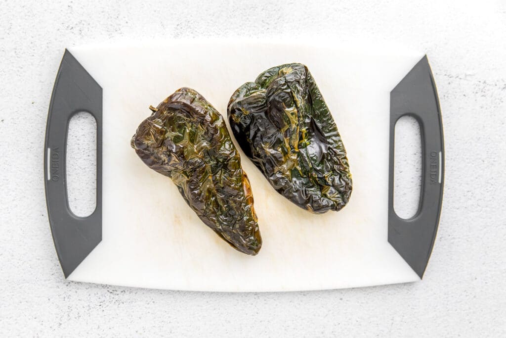 two roasted poblano peppers on a white cutting board