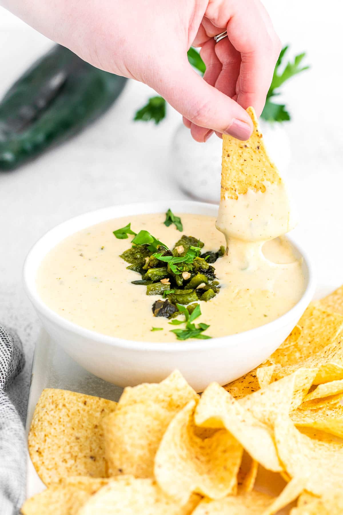 a white bowl with poblano queso dip wit a tortilla chip being dipped into