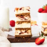 closeup of a stack of four strawberry cheesecake bars on a wood cutting board and white parchment paper