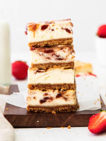 closeup of a stack of four strawberry cheesecake bars on a wood cutting board and white parchment paper