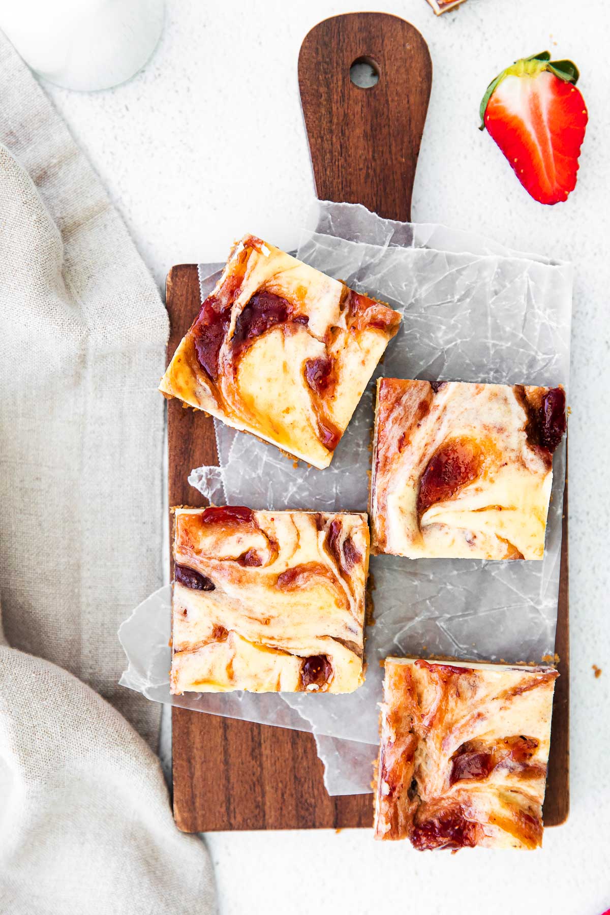 four strawberry cheesecake bars on a wood cutting board and white parchment paper