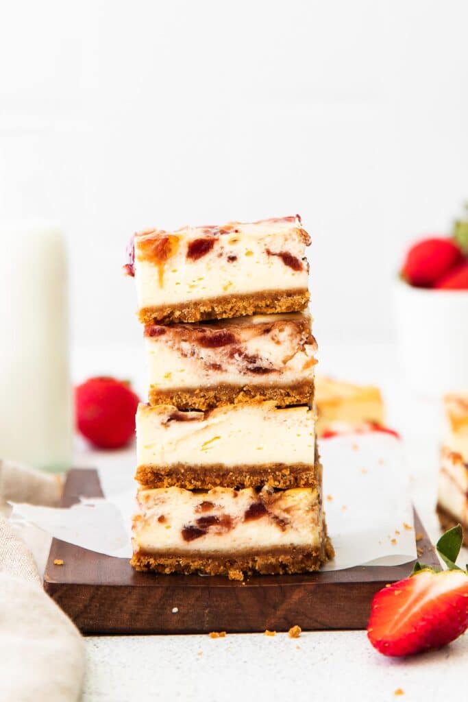 closeup of a stack of four strawberry cheesecake bars on a wood cutting board with fresh strawberries