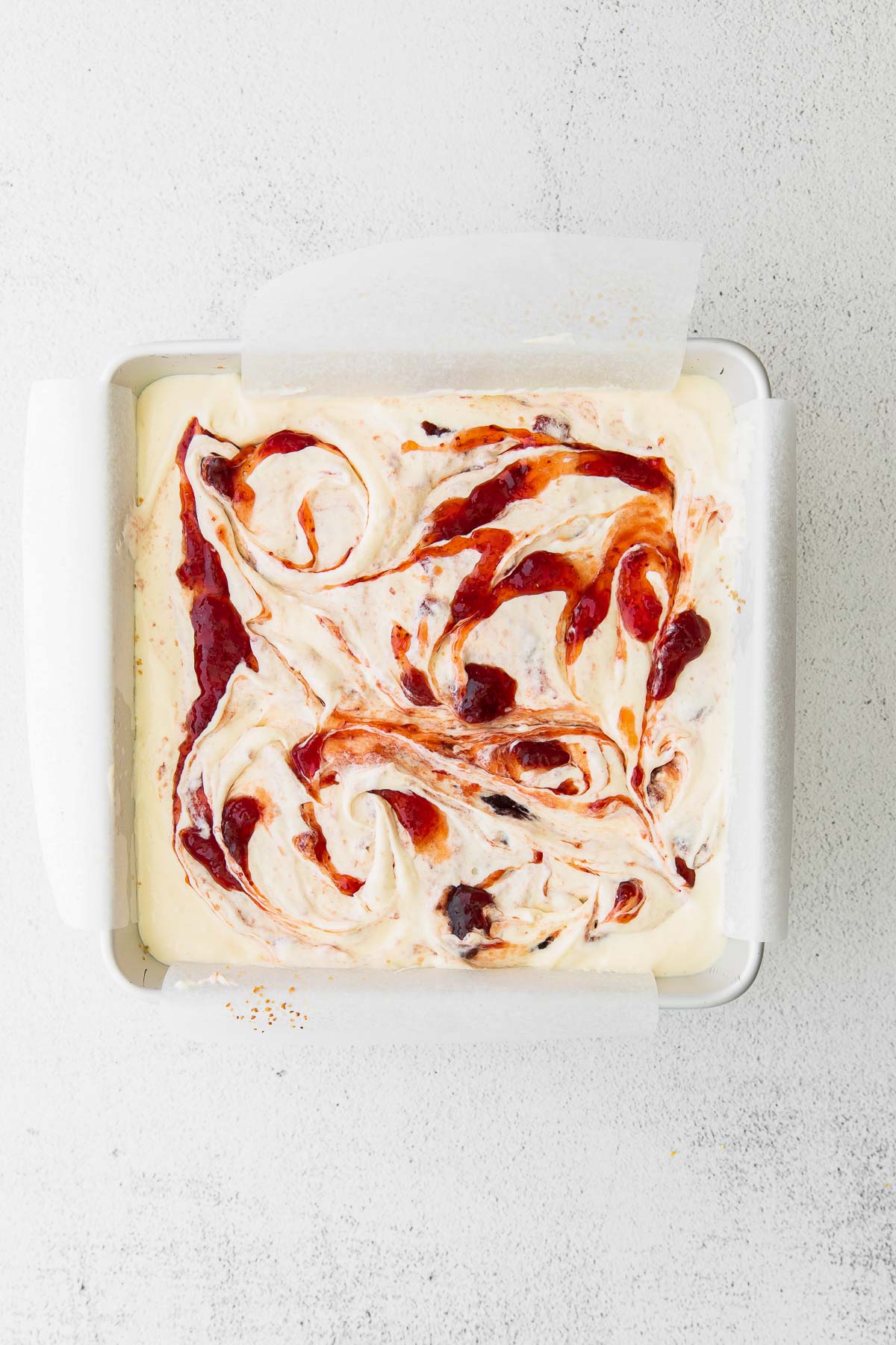 square baking dish with strawberry jam swirled into cheesecake bars batter
