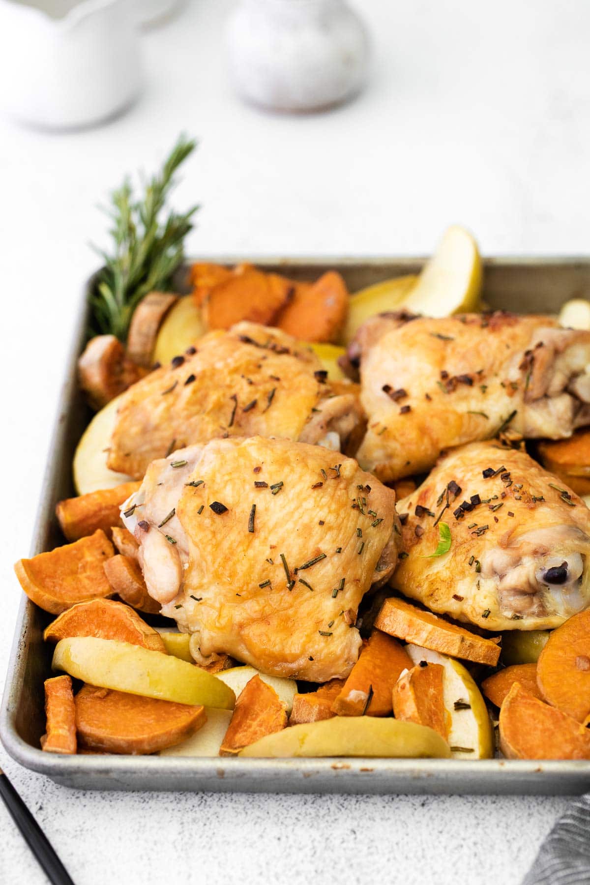 closeup of a sheet pan with sweet potatoes, apple slices and chicken thighs