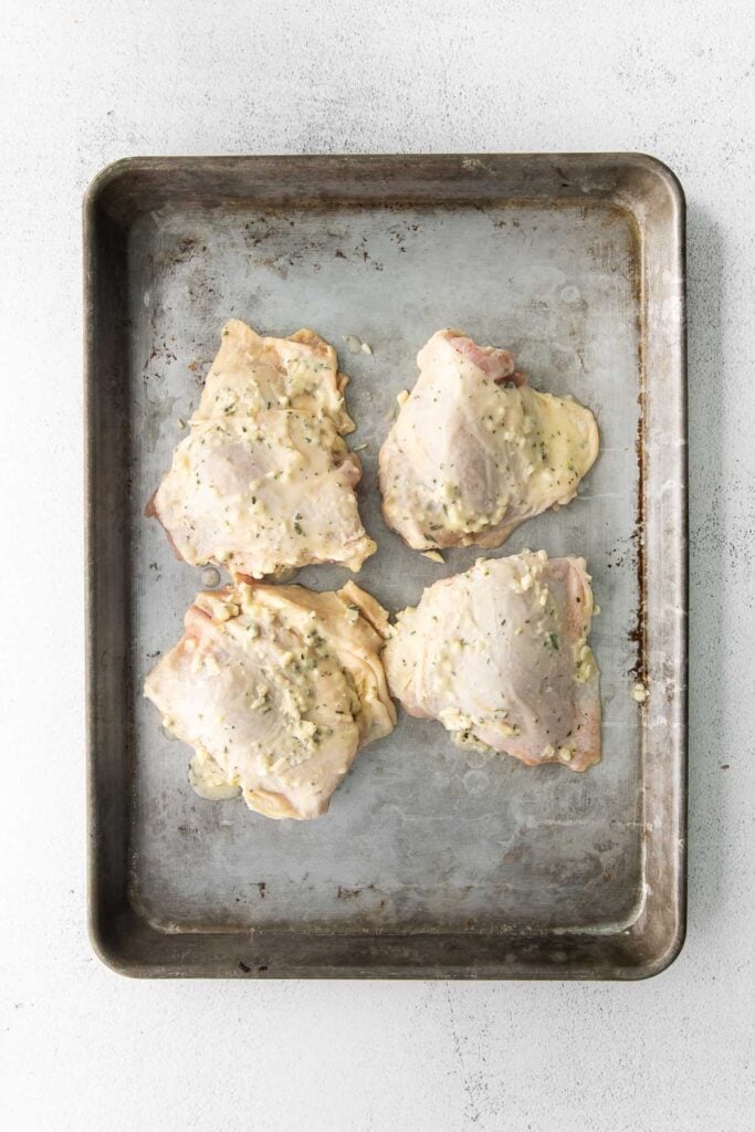 four raw chicken thighs on a sheet pan
