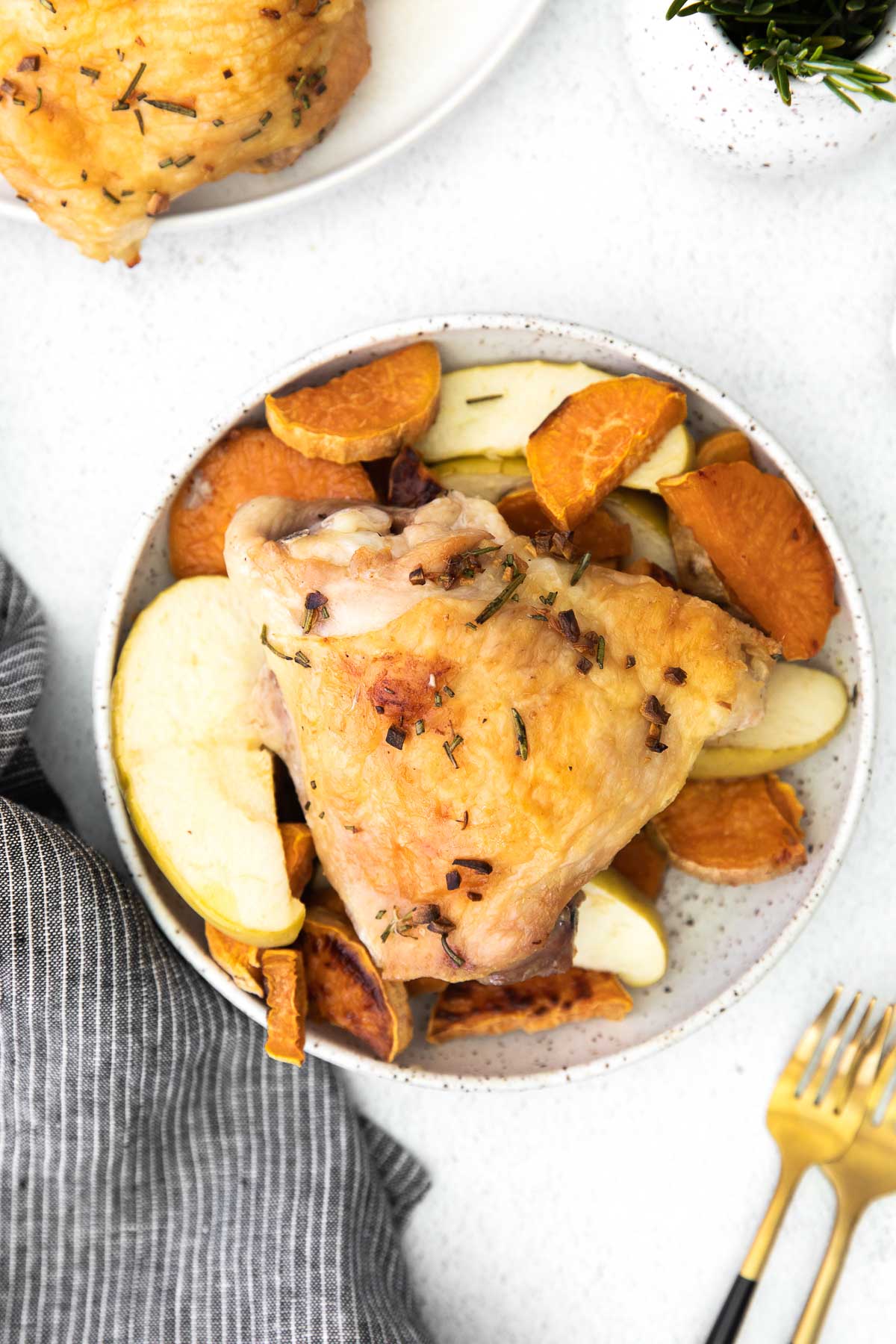 white bowl with sweet potatoes and apple slices with a baked chicken thigh on top