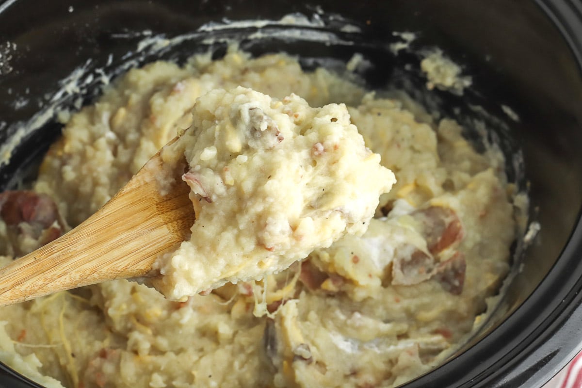 wood spoon of loaded mashed potatoes in a black slow cooker