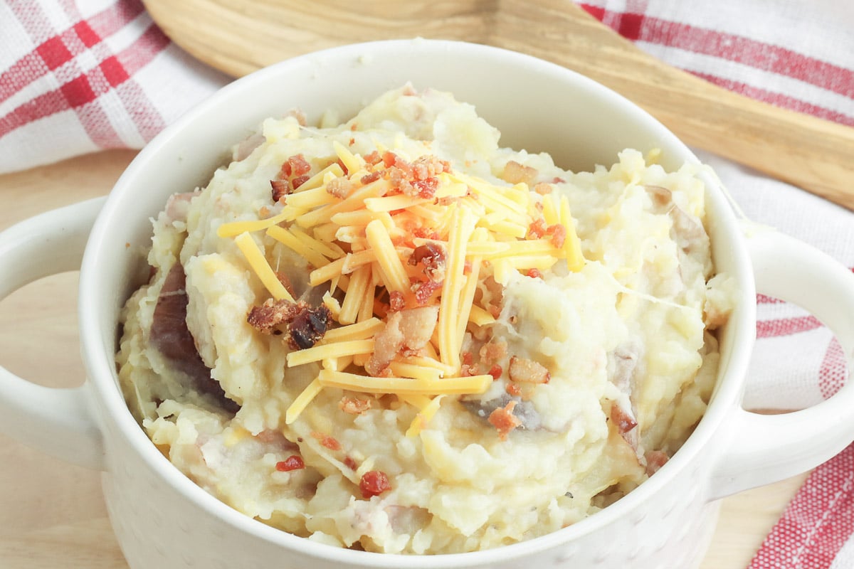 mashed potatoes in a white bowl with shredded cheese and bacon on top