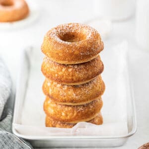 stack of five apple cider donuts on silver baking sheet with parchment paper