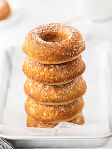 stack of five apple cider donuts on silver baking sheet with parchment paper