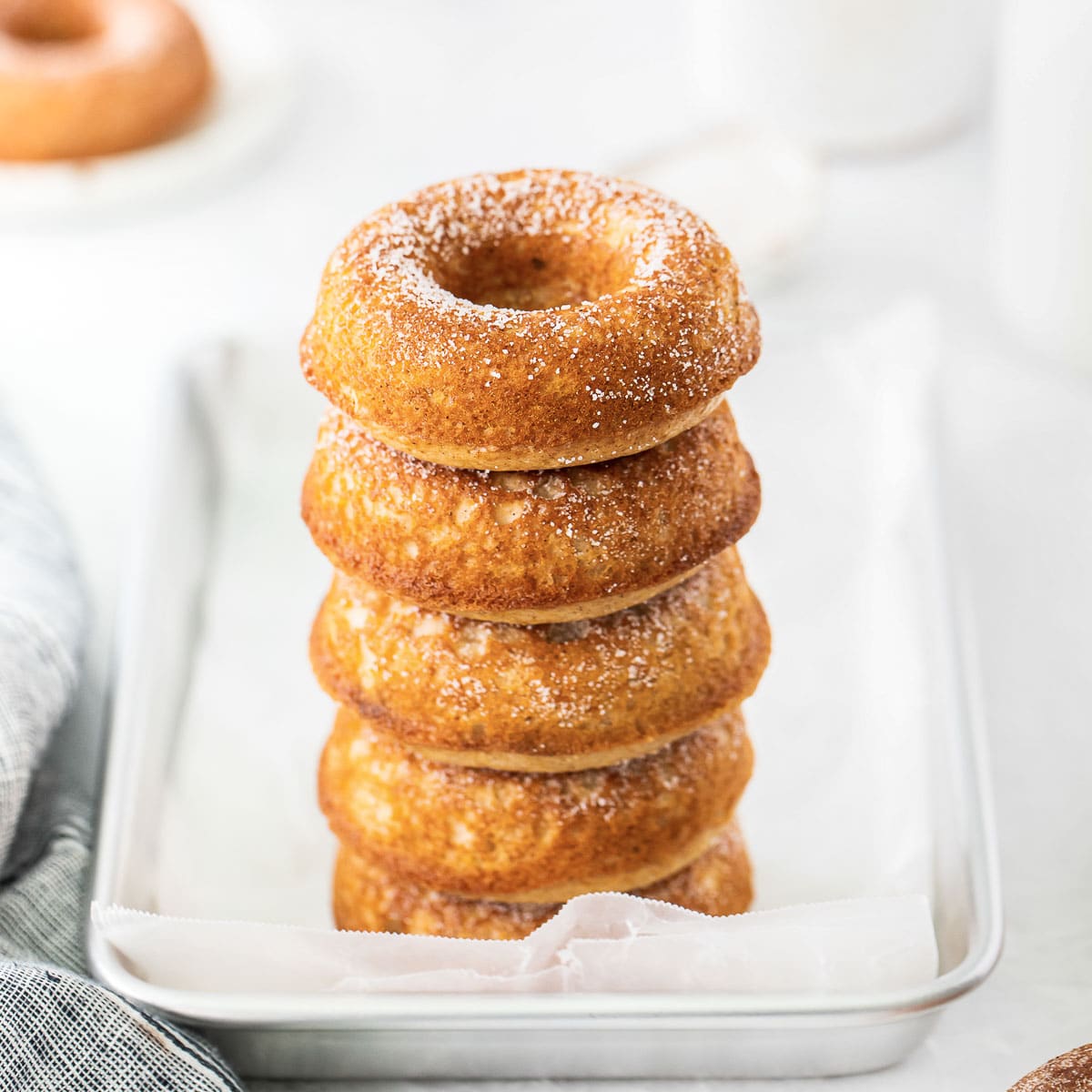 stack of five apple cider donuts on silver baking sheet with parchment paper