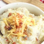 bowl full of mashed potatoes topped with shredded cheese and bacon bits