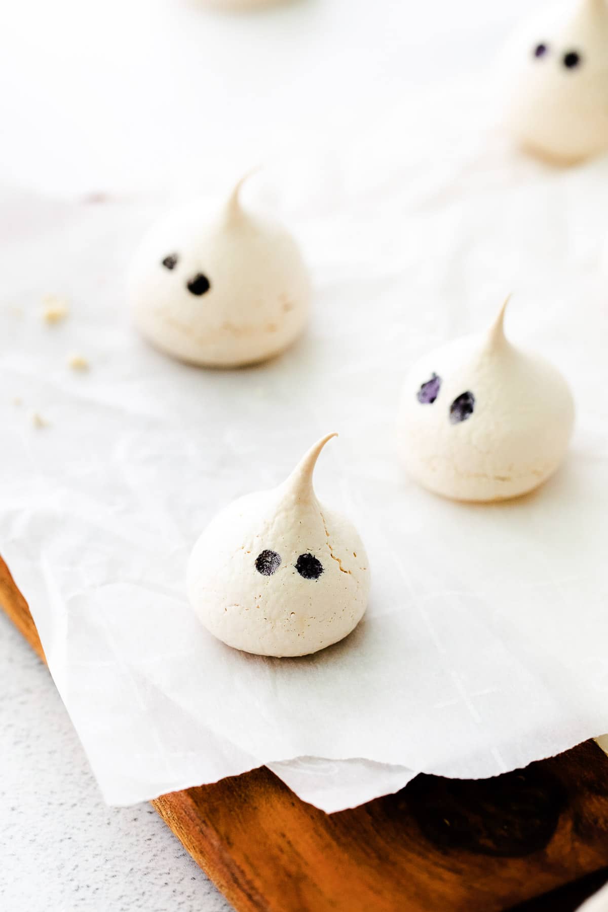 three ghost shaped meringues on white parchment paper on a wood cutting board