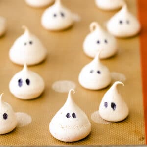 several little ghost shaped meringue cookies on a brown baking mat