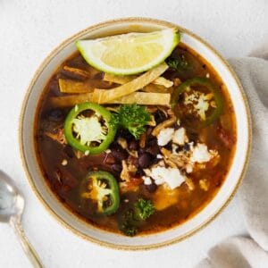 closeup of a white bowl of soup with chicken, black beans, tortilla strips and sliced jalapenos