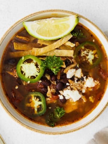 closeup of a white bowl of soup with chicken, black beans, tortilla strips and sliced jalapenos