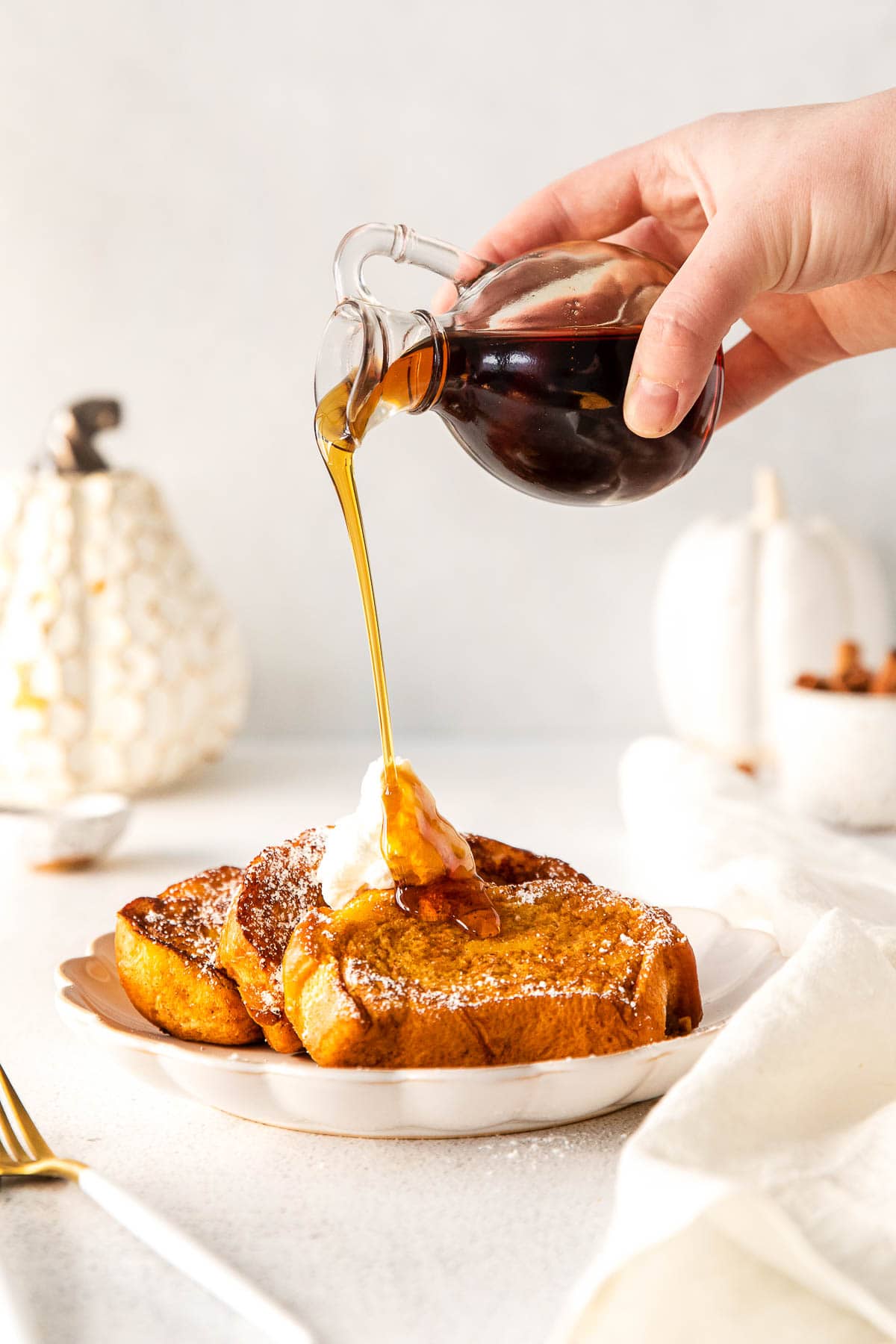 syrup being poured over three slices of french toast topped with butter and powdered sugar
