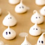 several white meringue cookies in ghost shapes on a baking sheet