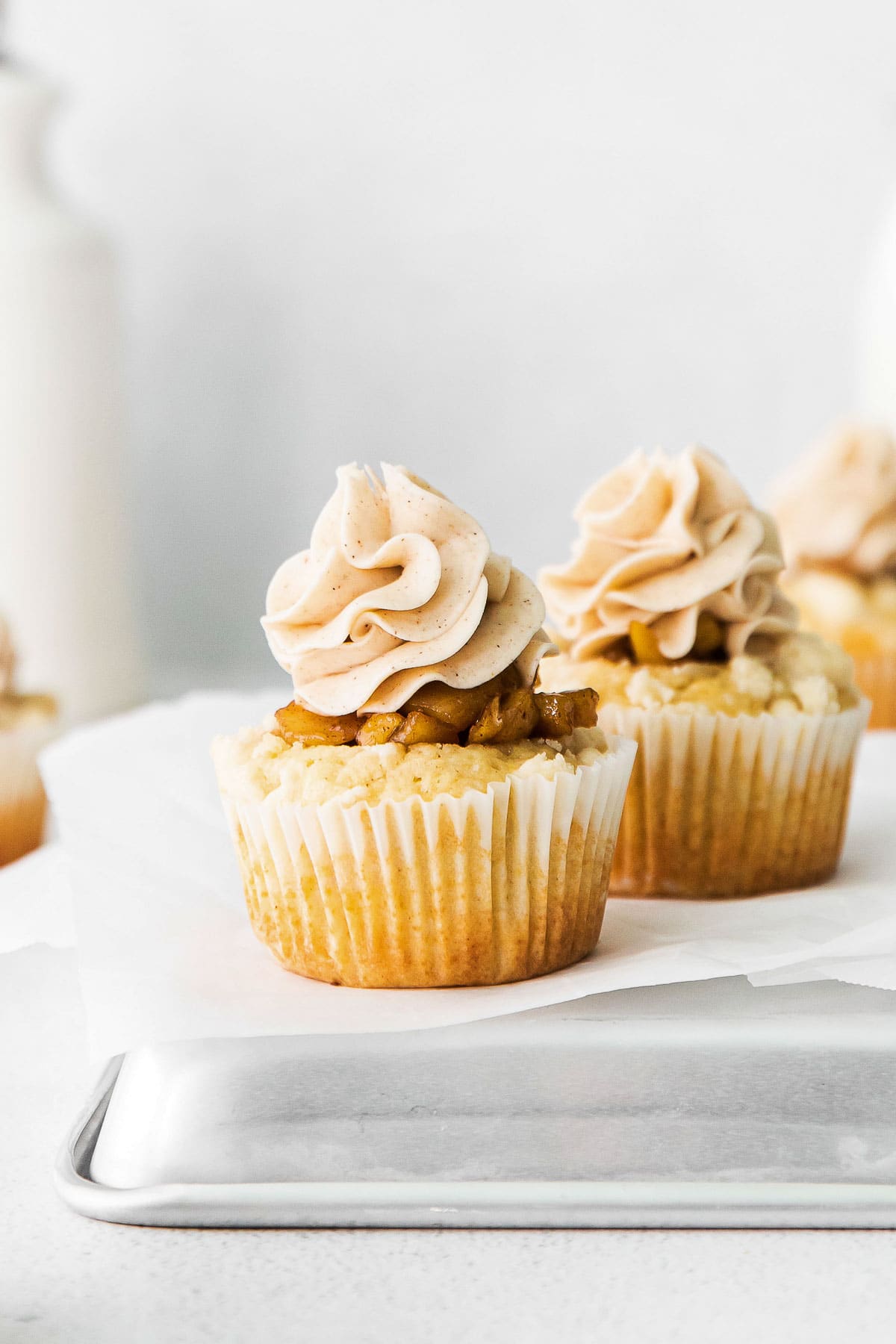 closeup of a vanilla cupcake topped with diced apple pie filling and buttercream frosting