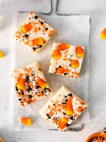 closeup of 3 squares of white fudge with candy corn and orange and black sprinkles