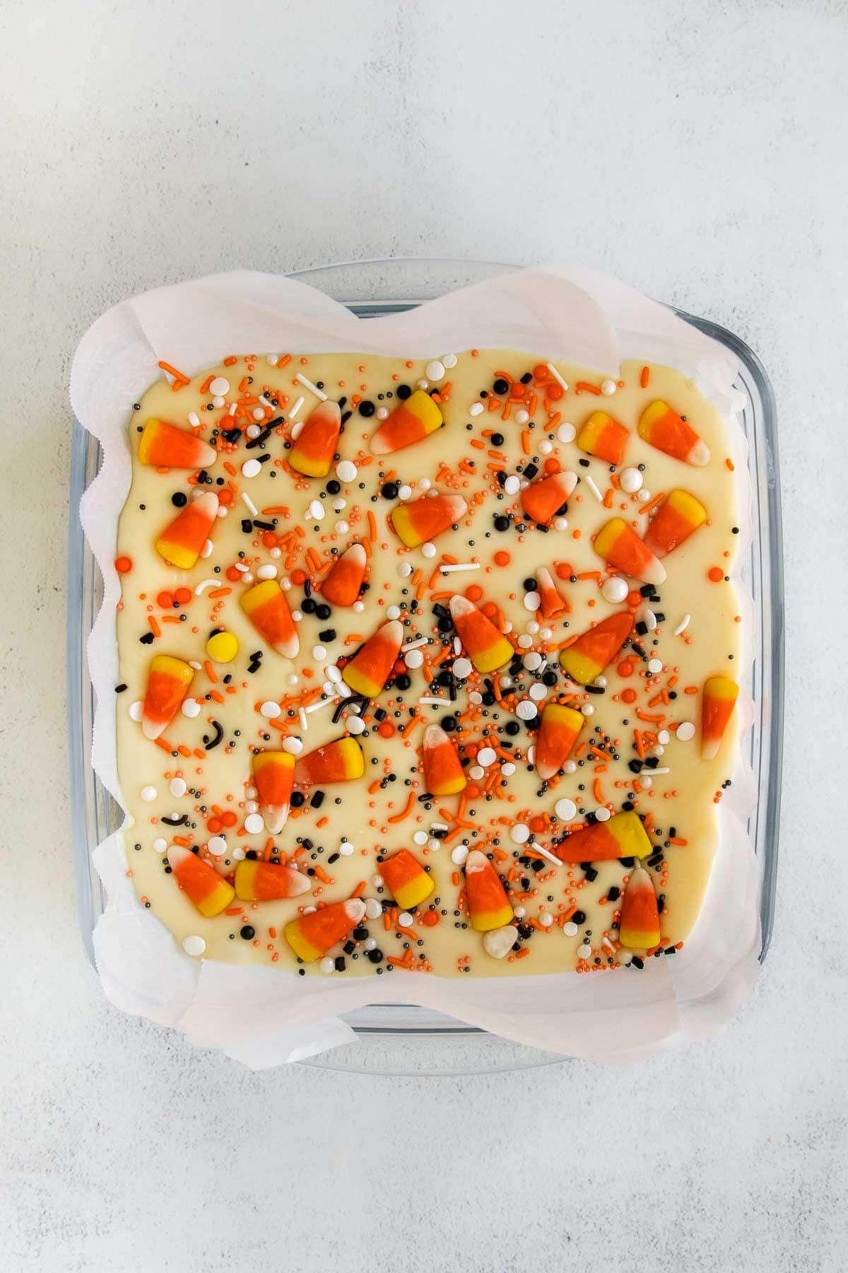 closeup of square glass baking dish with vanilla fudge topped with candy corn and halloween colored sprinkles
