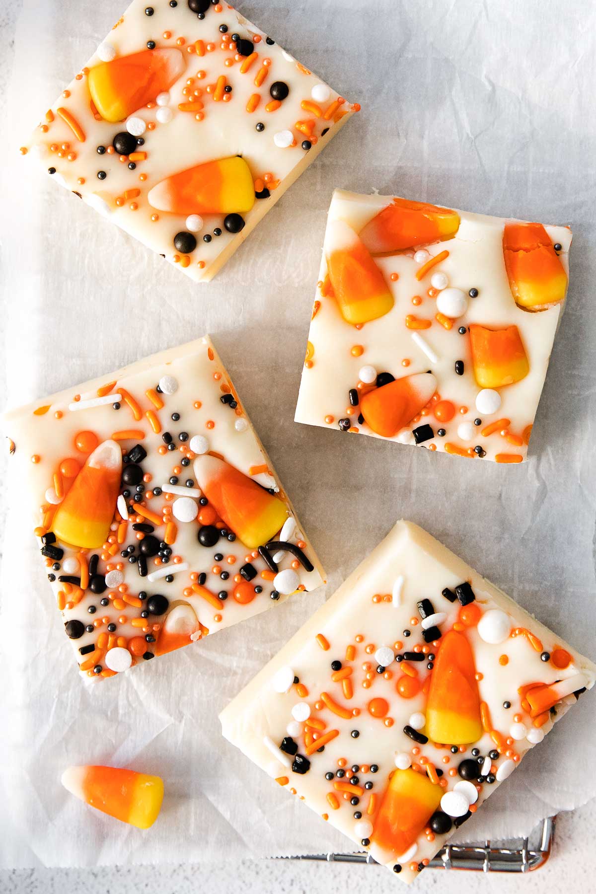 closeup of three squares of halloween vanilla fudge topped with candy corn and black orange and white sprinkles