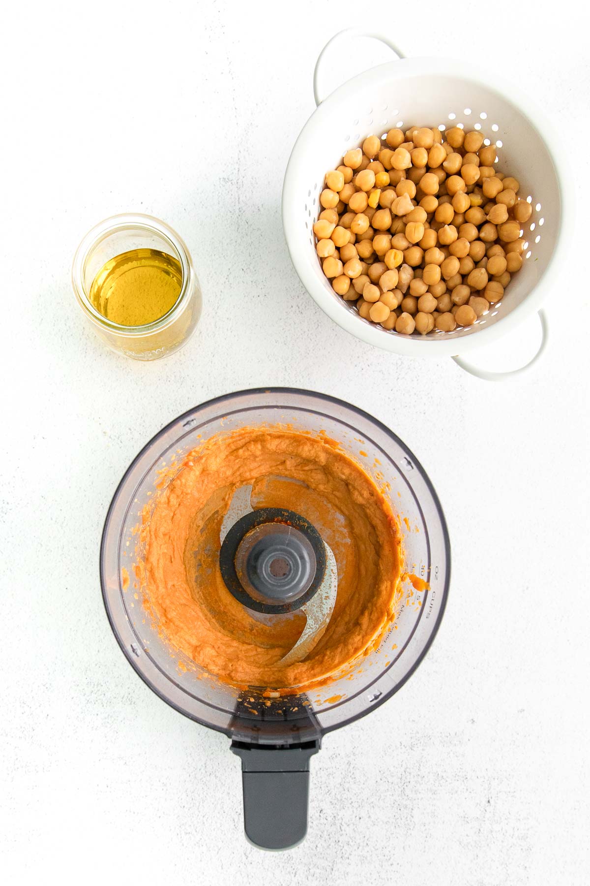 pumpkin puree in a food processor and a white colander of chickpeas and a little bowls of olive oil