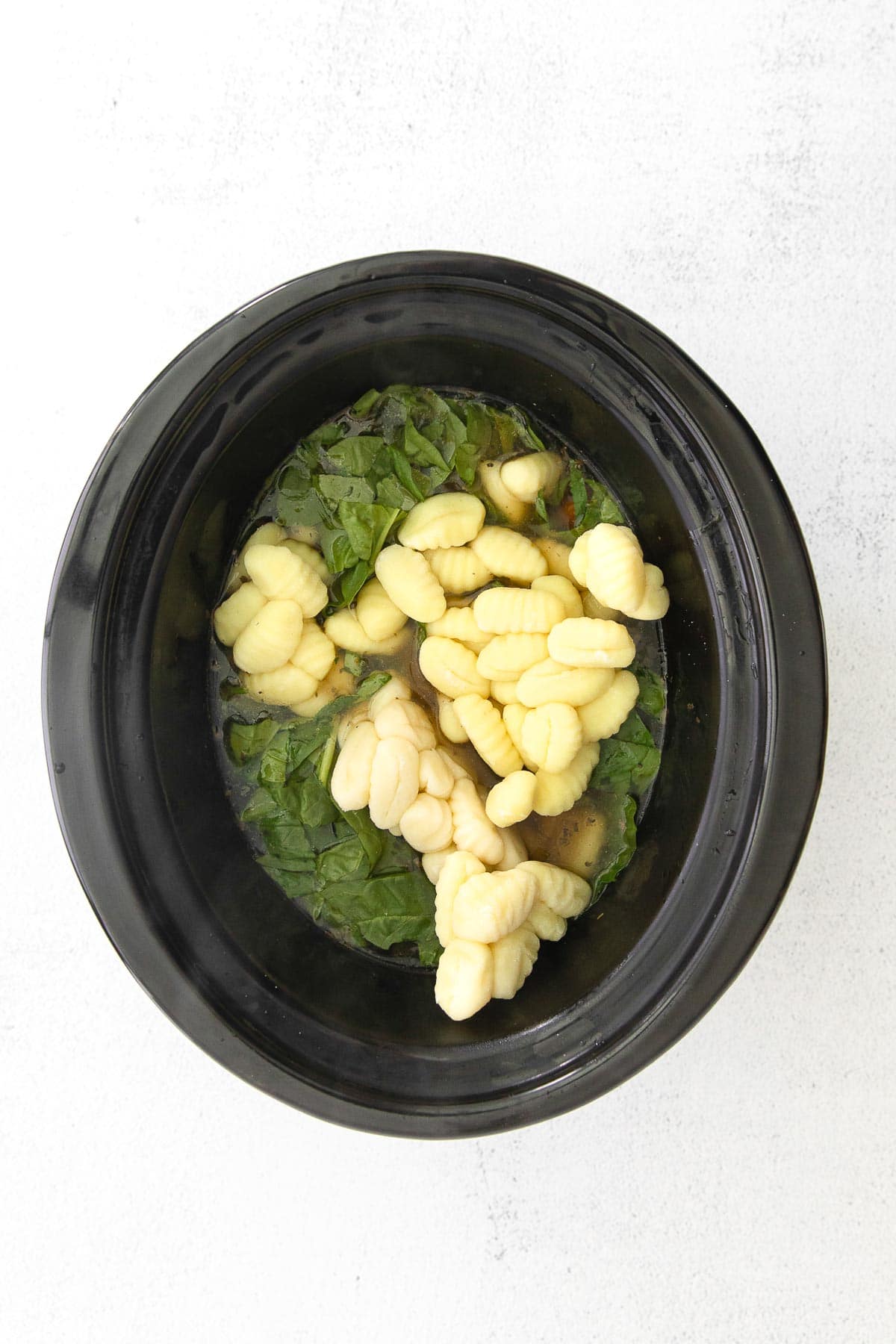 gnocchi and spinach in soup broth in a black crockpot