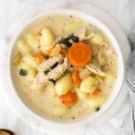 closeup of a white bowl filled with creamy chicken gnocchi soup with carrots and spinach