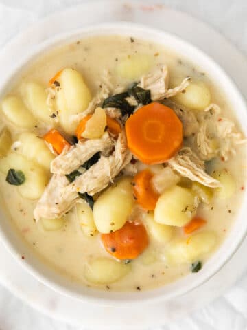 closeup of a white bowl filled with creamy chicken gnocchi soup with carrots and spinach