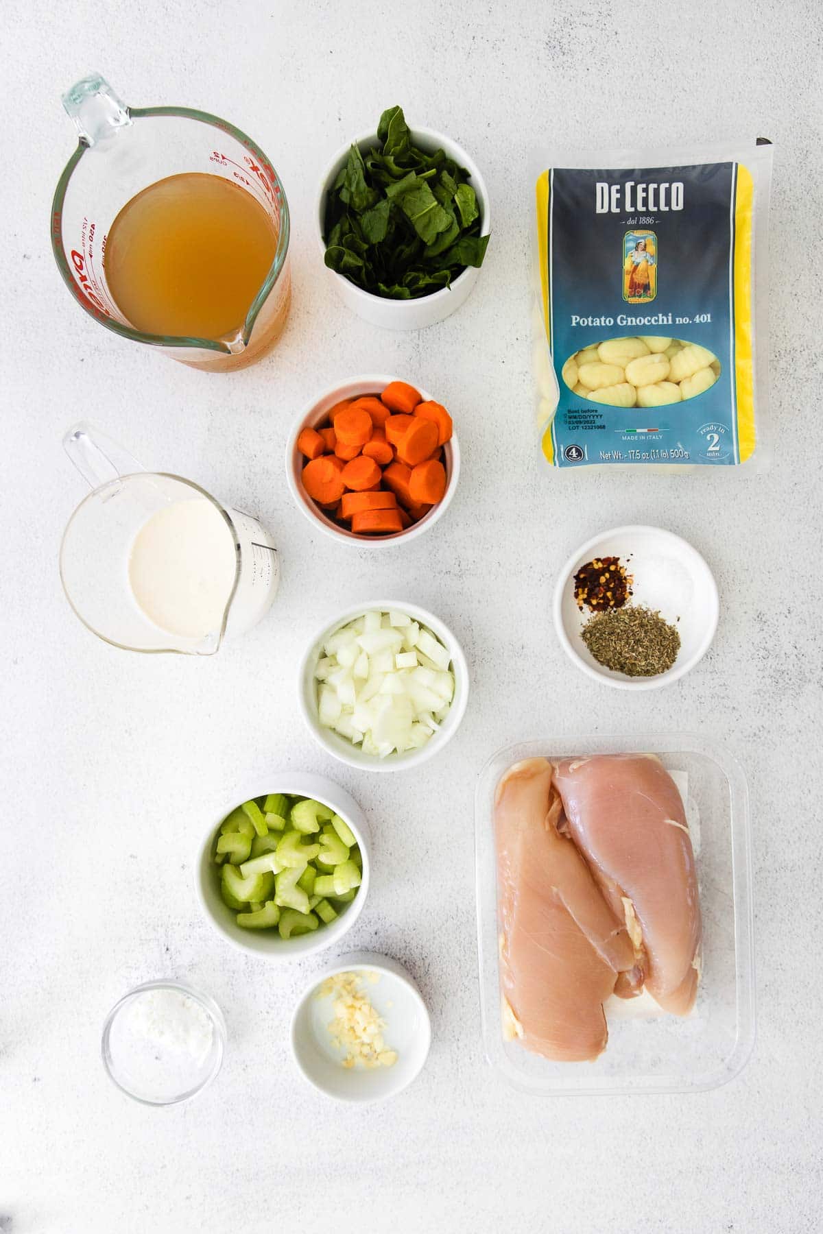 several small white bowls with ingredients for soup-minced garlic, diced celery, sliced carrots, spinach, salt, heavy cream, two chicken breasts and a box a gnocchi