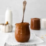 small glass jar of homemade pumpkin butter with a spoon sticking out surrounded by small jar of milk and white pumpkin