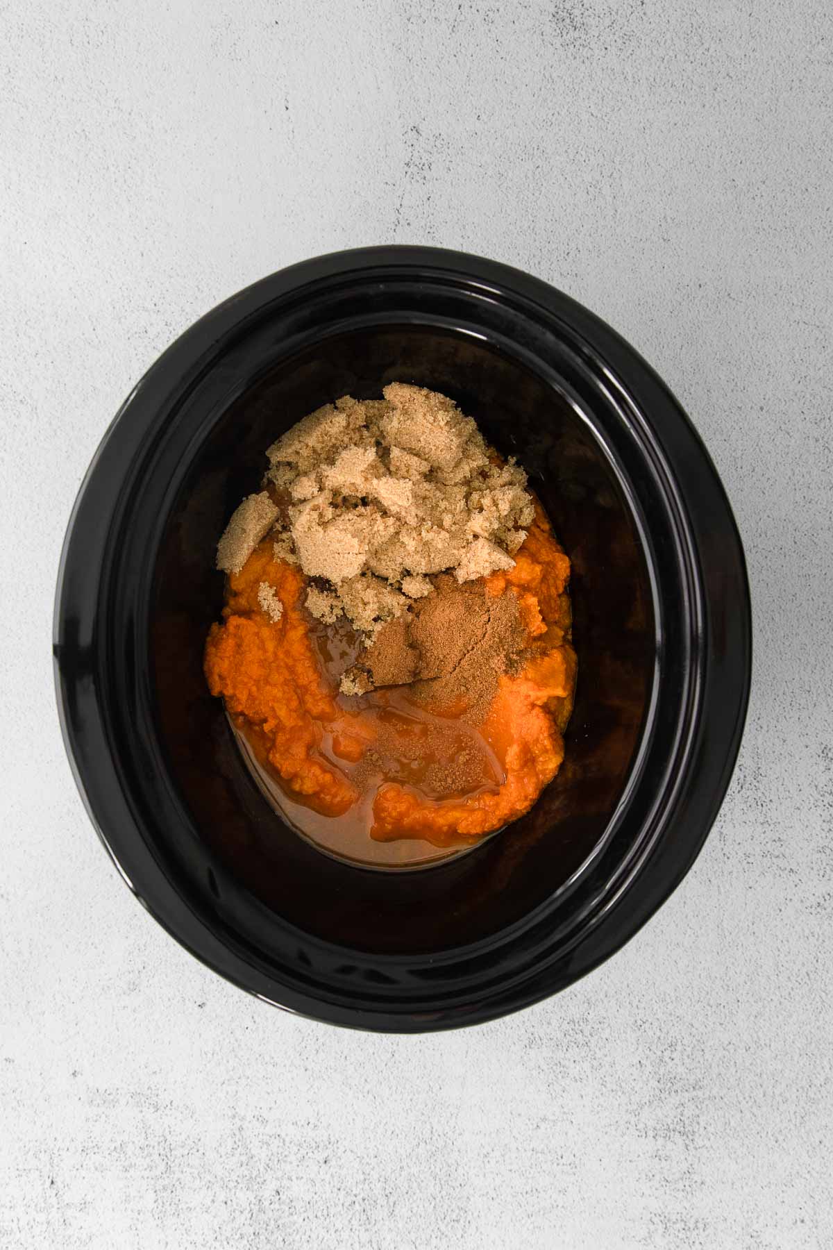 black slow cooker with pumpkin, brown sugar, and spices