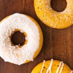 three pumpkin donuts with drizzle and icing on a dark wood cutting board