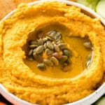 white bowl with pumpkin hummus topped with olive oil and pumpkin seeds