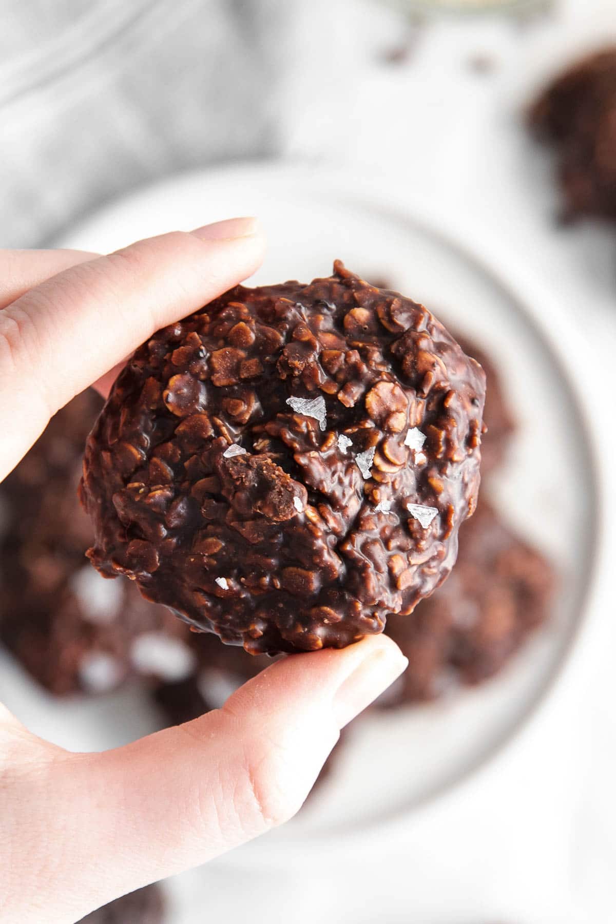 closeup of womans hand holding a chocolate oatmeal cookie