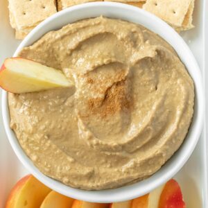 closeup of hummus in a white bowl with an apple slice dipped in