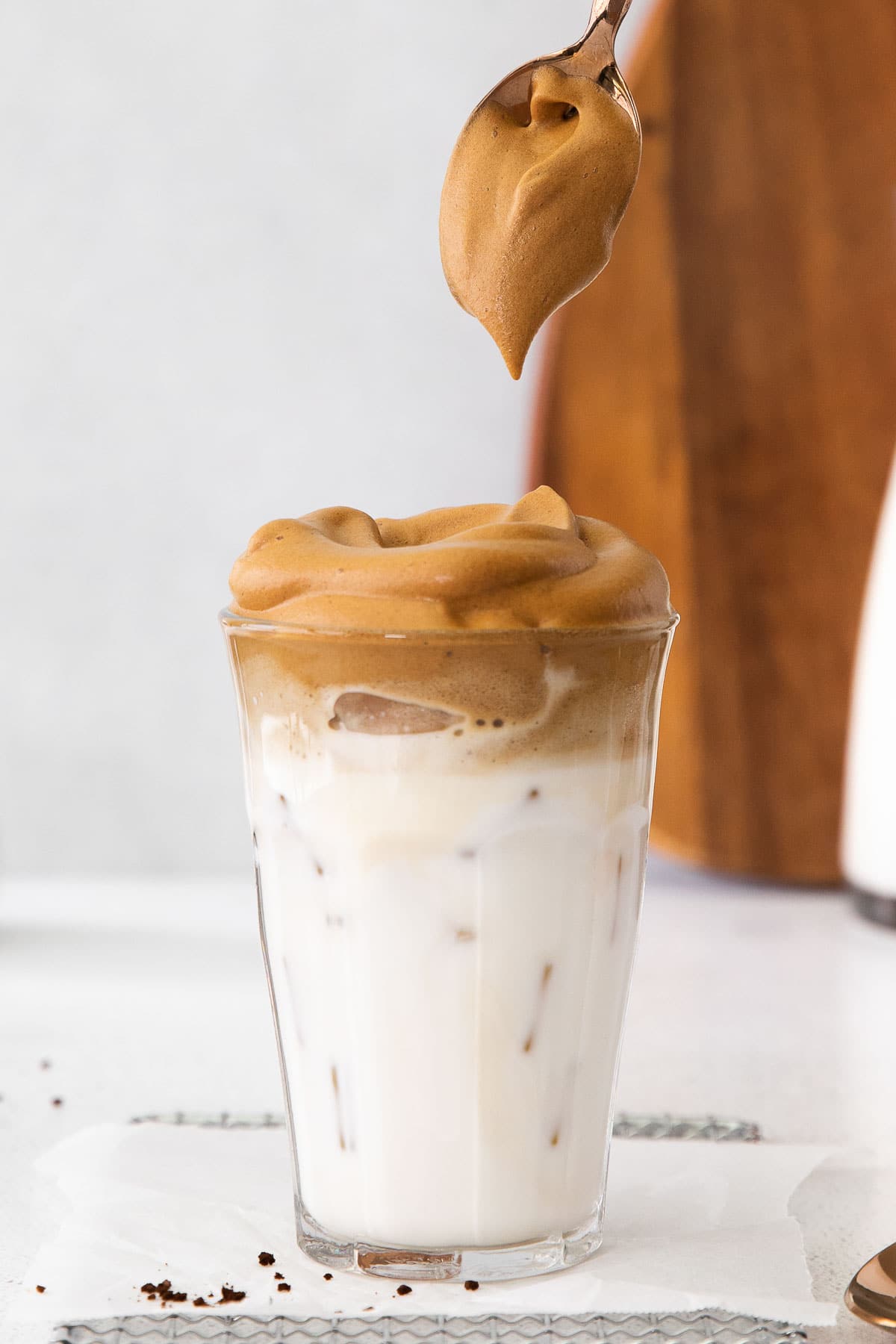 closeup of glass of whipped coffee over milk with spoonful over top
