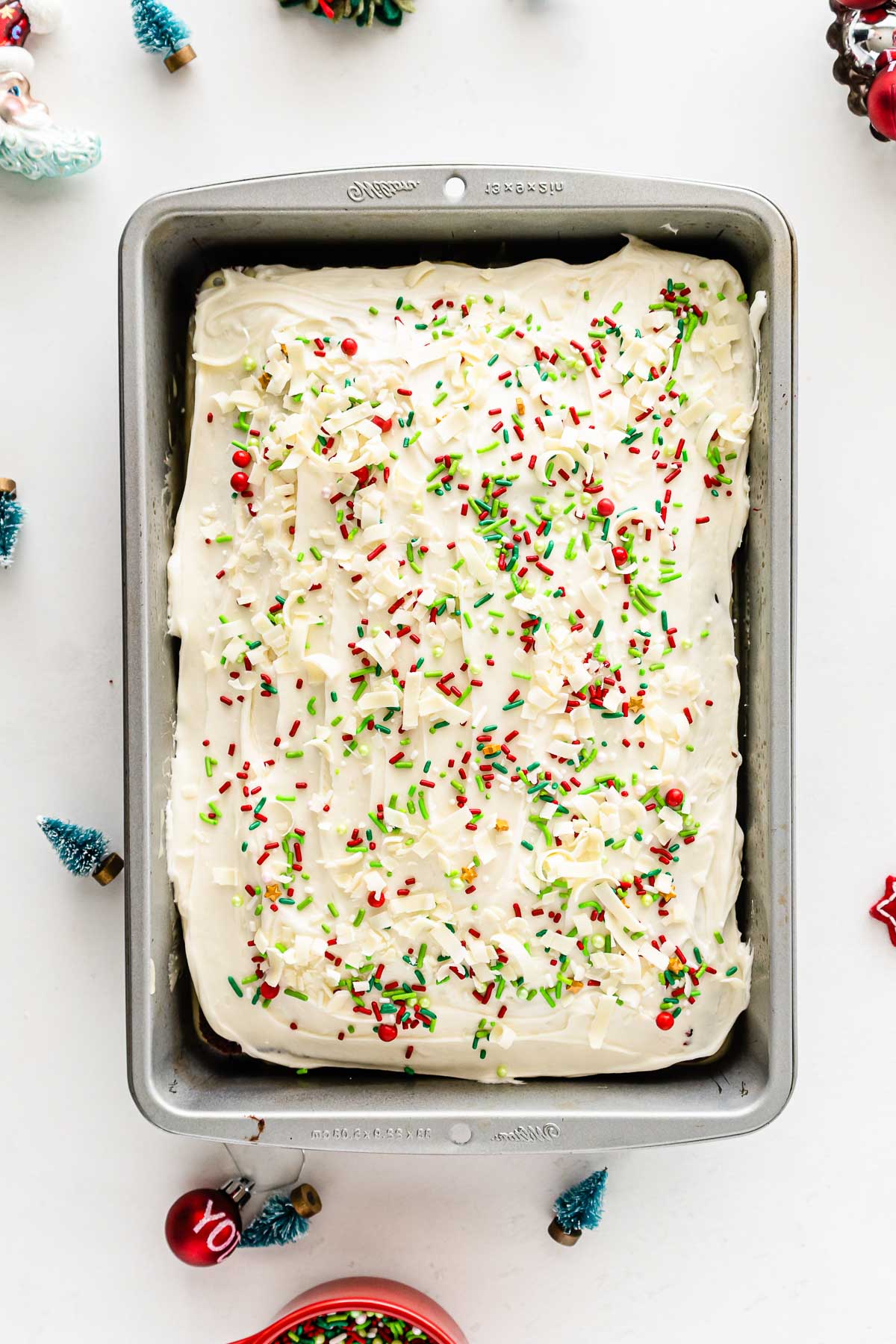 rectangle baking pan with a cake topped with cream cheese frosting with Christmas sprinkles