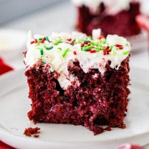 closeup of a square slice of red velvet cake poke cake with white icing and red and green Christmas sprinkles