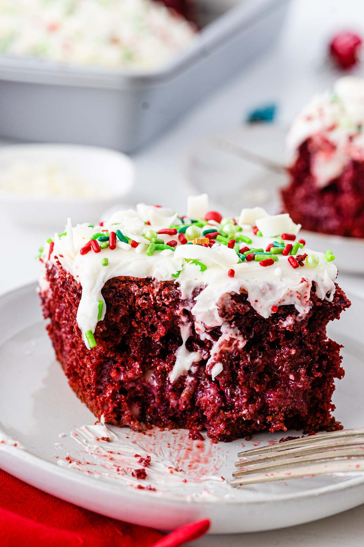 closeup of the inside of a slice of red velvet poke cake with cream cheese icing on a white plate