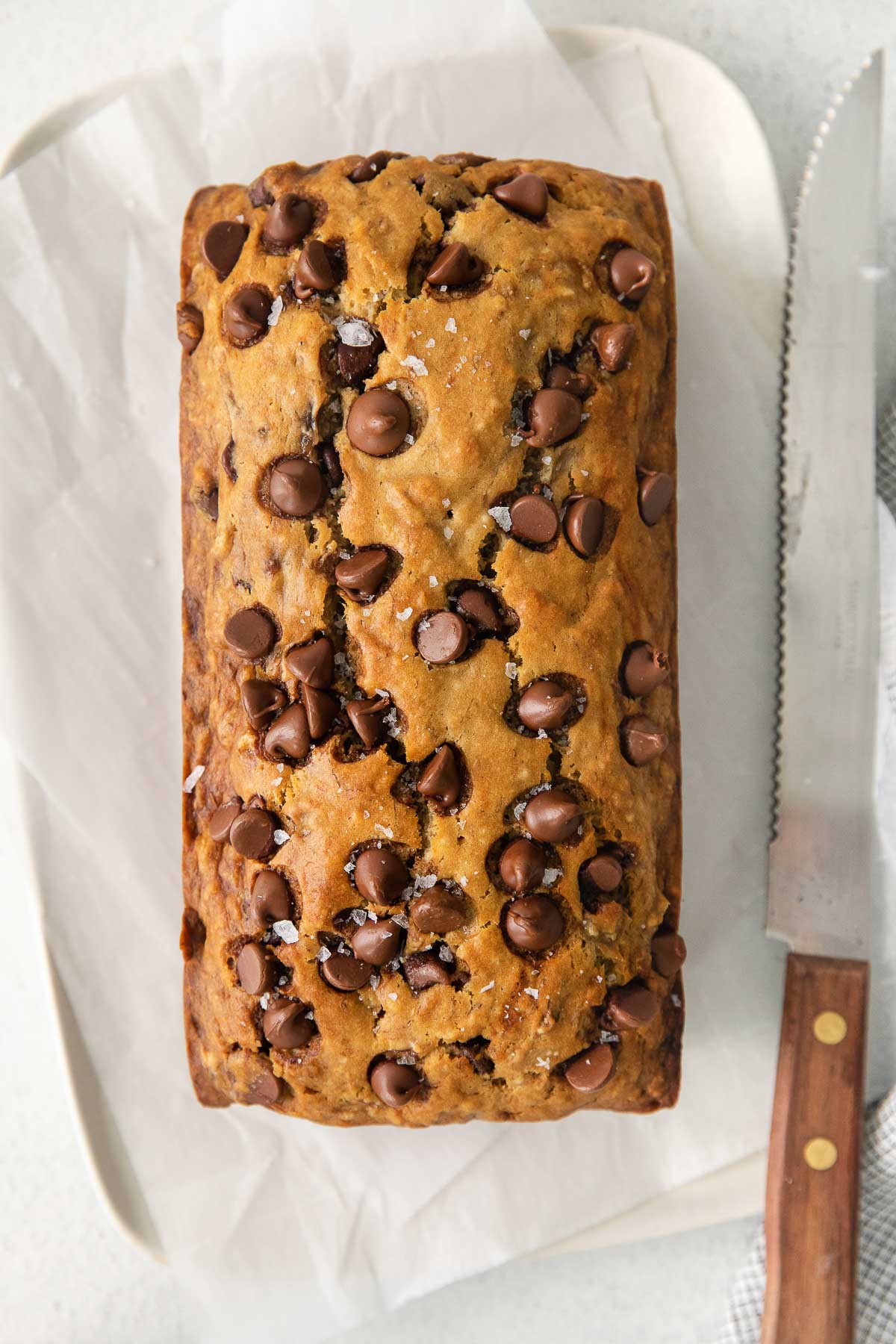 closeup of a loaf of chocolate chip banana bread on parchment paper with a knife with wood handle