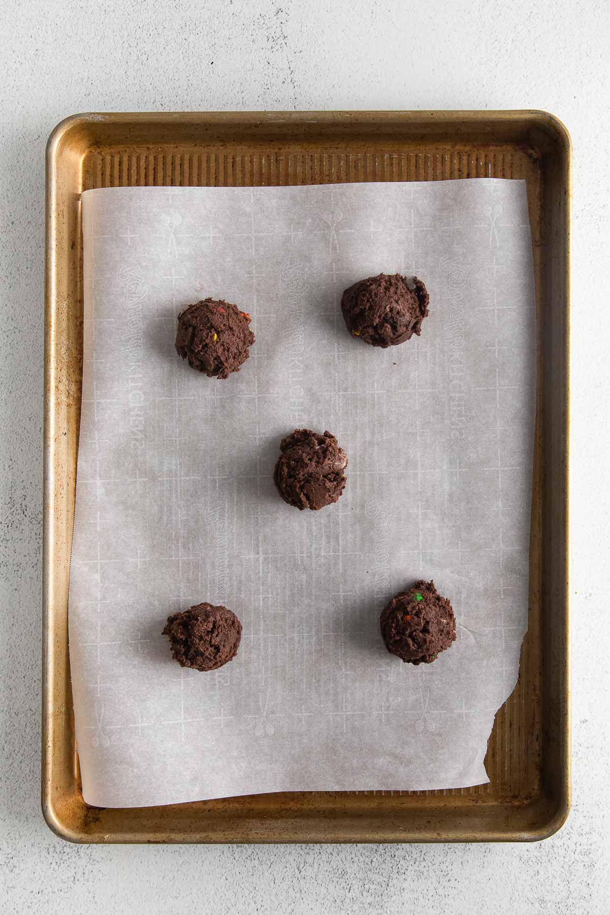 five chocolate cookie dough scoops on a parchment paper lined baking sheet