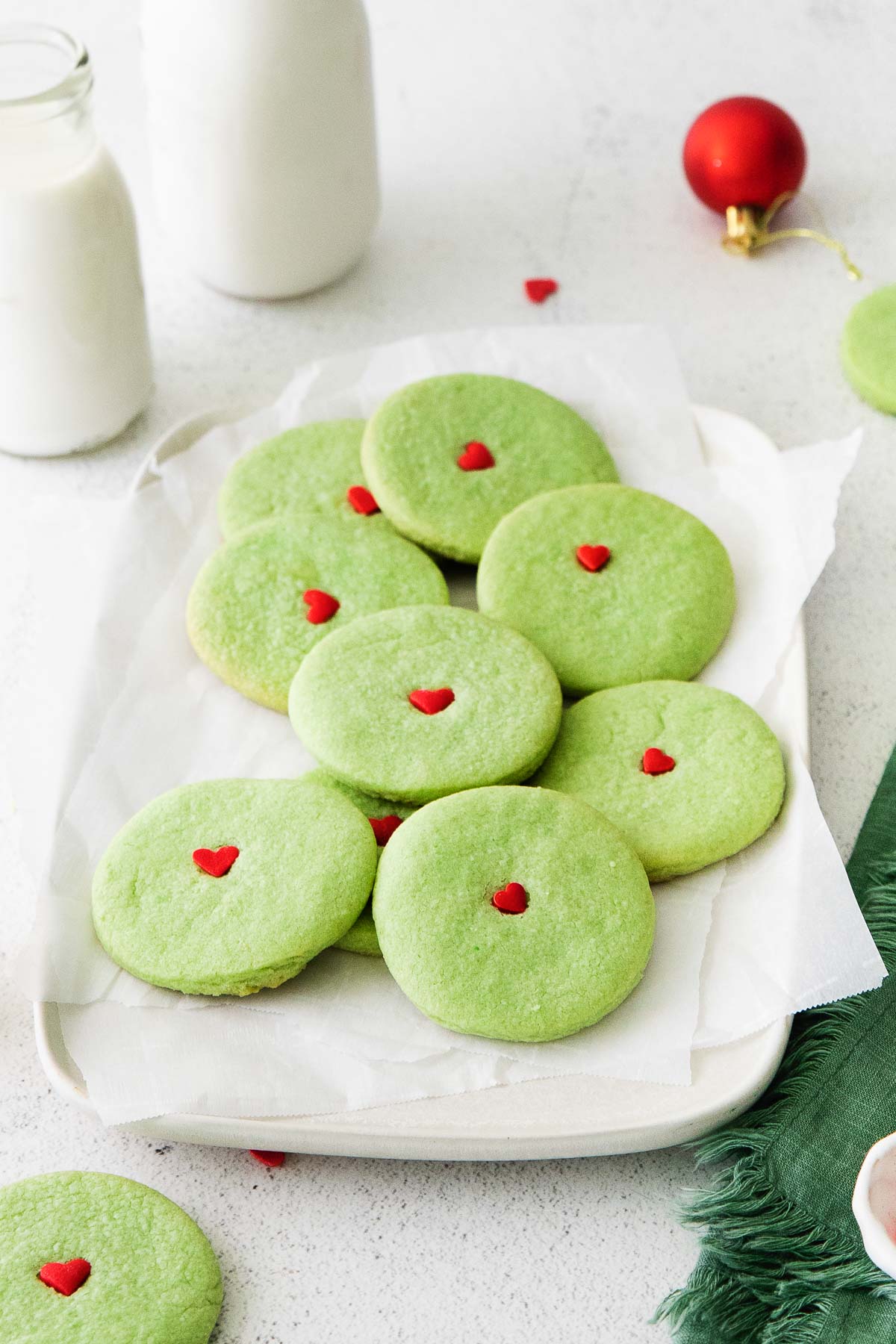a white rectangle plate full of green cookies with a red heart on each one